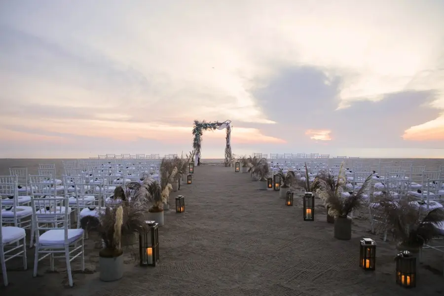 Beachfront ceremony aisle lined with pampas grass and lanterns at sunset